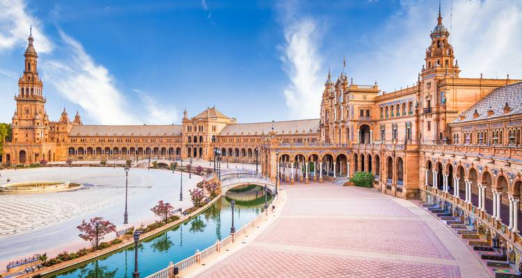 An expansive plaza with a canal and detailed architecture under a blue sky.