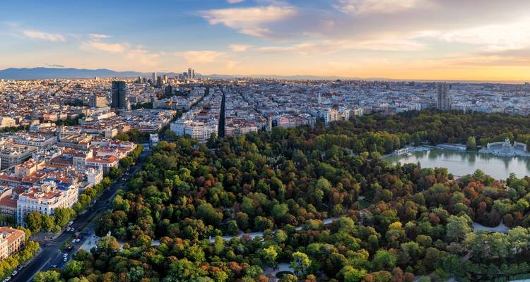 Aerial view of a city with a large park and water features, with a sunset sky.