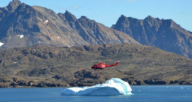 Un hélicoptère volant au-dessus d'un iceberg avec des montagnes en arrière-plan.