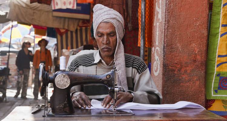 Homme cousant des vêtements avec une vieille machine à coudre dans un marché.