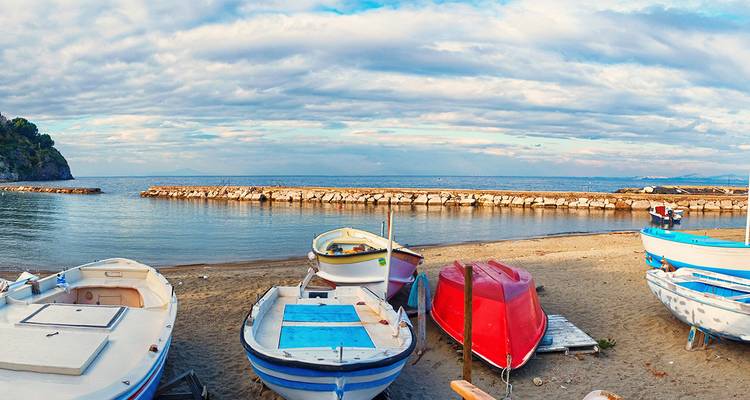 Des bateaux colorés sur une plage de sable avec une digue rocheuse.