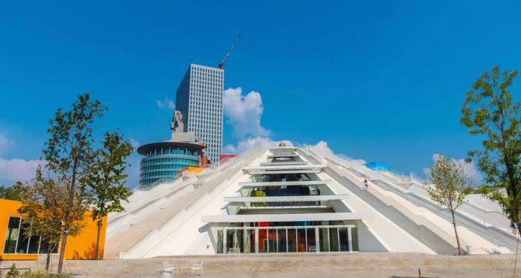 Bâtiment blanc moderne en forme de pyramide d'un centre culturel à usage mixte situé sur un ciel bleu dégagé et flanqué d'une tour de grande hauteur.