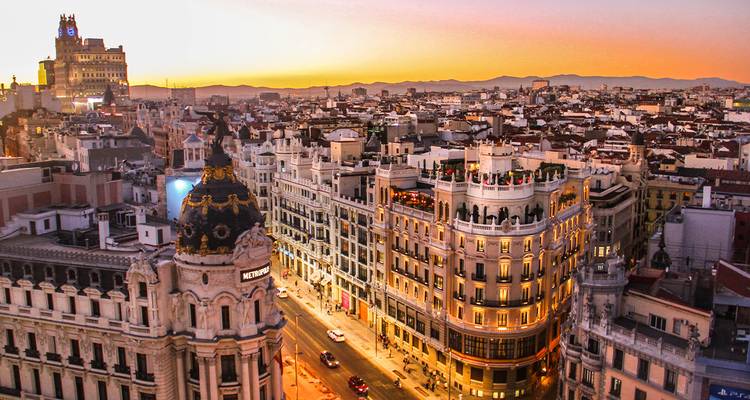 La Gran Vía de Madrid resplendit au coucher du soleil avec le dôme du bâtiment Metropolis et les lumières de la ville se détachant contre les ciels orangés.