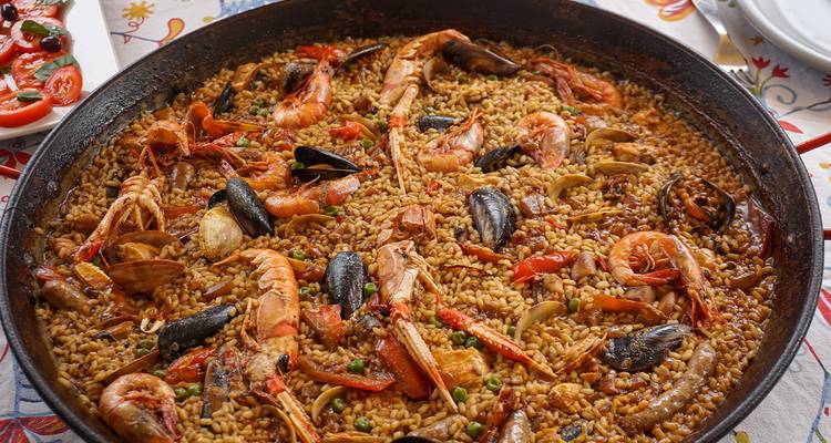 Une poêle fumante de paella aux fruits de mer débordant de crevettes, de moules et de riz repose sur une table carrelée.