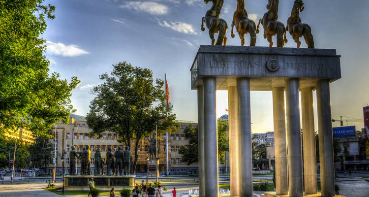 Monumento con cuatro caballos de bronce encima de columnas altas en una plaza de la ciudad de Skopje durante la tarde