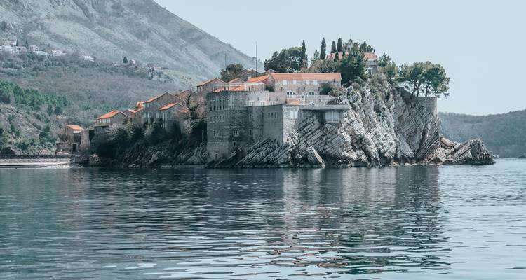 L'île fortifiée emblématique de Sveti Stefan se reflète sur les eaux calmes de l'Adriatique sous un ciel voilé.