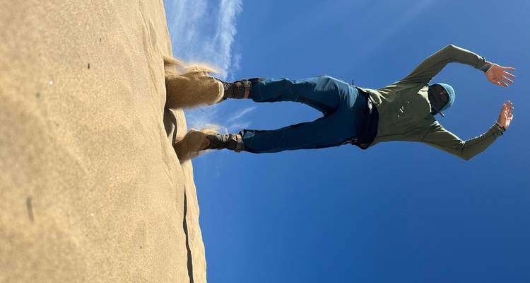 Personne sautant sur une dune de sable contre un ciel bleu vif.