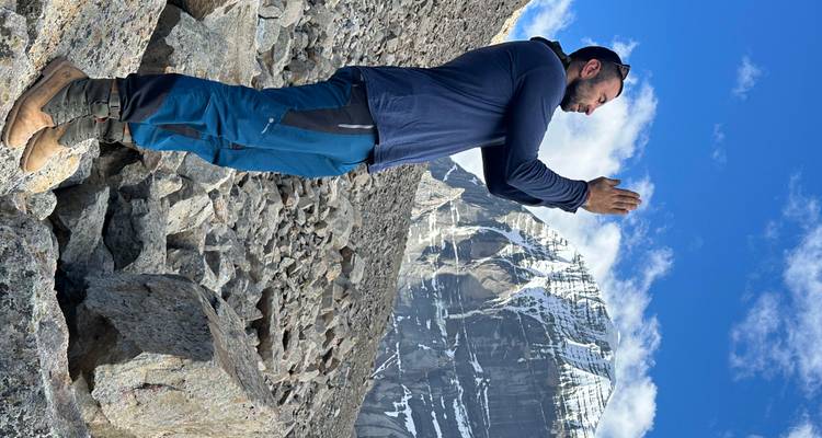 Homme priant les mains levées vers une montagne enneigée.