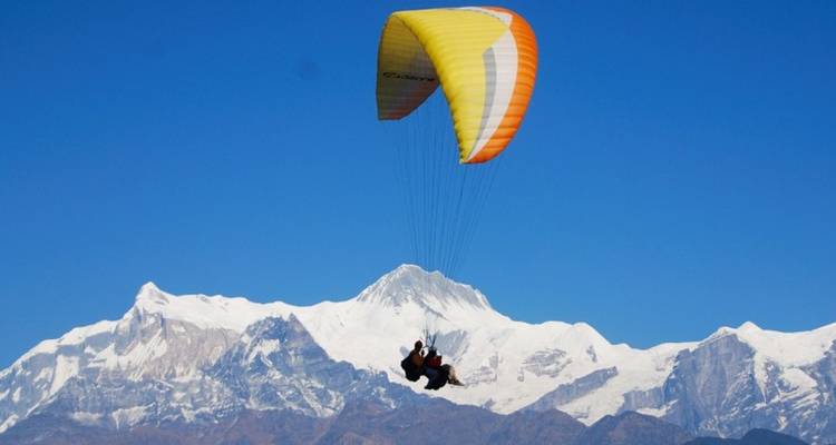 Persona haciendo parapente con montañas nevadas al fondo.