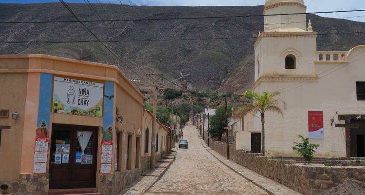 Scène de rue dans une petite ville avec une église sur la droite et des montagnes en arrière-plan.