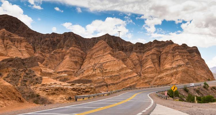 Route sinueuse à travers les montagnes désertiques avec un ciel bleu.