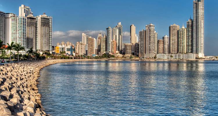 Moderne Skyline von Panama-Stadt, die sich über die Bucht erhebt, mit ruhigem Wasser und steinerner Ufermauer im Vordergrund.