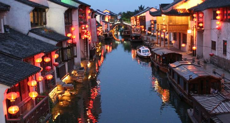 Lantern-lit water town canal at dusk with reflections of glowing reds and golds.