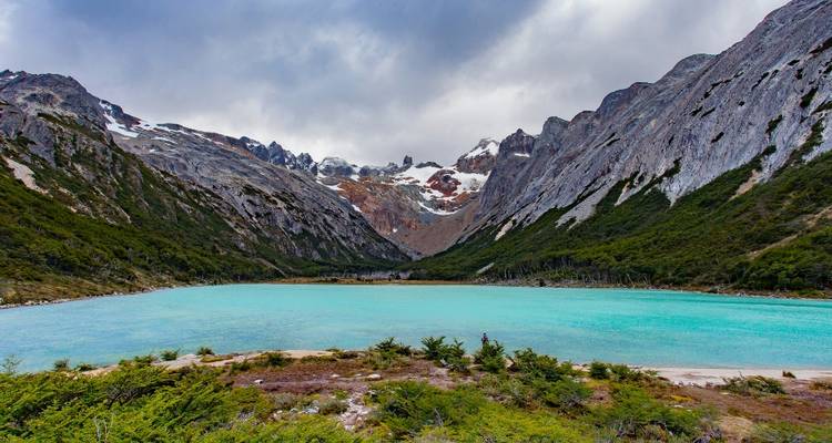 Lac turquoise entouré de montagnes sous un ciel nuageux.