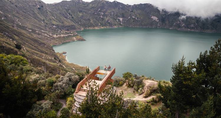 Una pareja de pie en una plataforma de observación con vista a un lago de cráter volcánico.