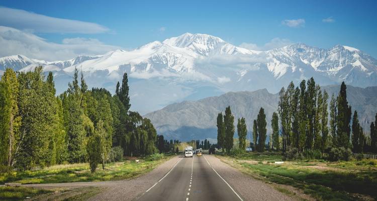 Une route ouverte mène vers des montagnes enneigées avec des arbres sur les côtés.