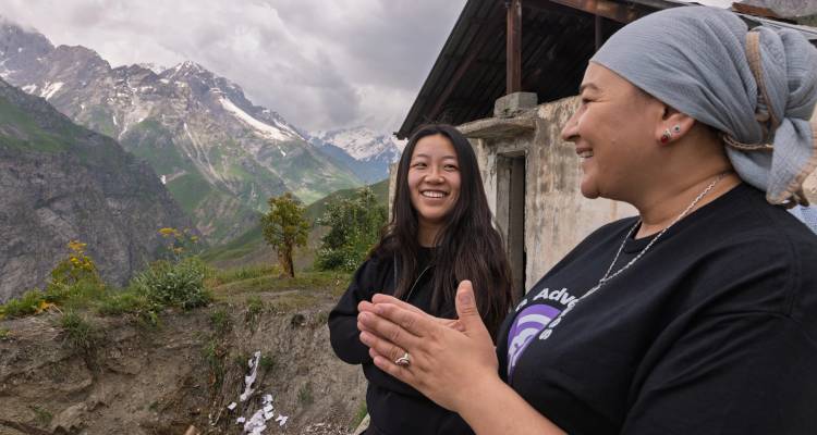 Deux voyageurs partagent un moment de rire avec les montagnes enneigées d'Asie centrale qui se dressent majestueusement derrière eux.