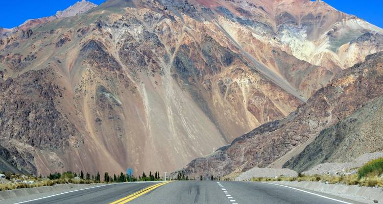 Formations rocheuses colorées le long d'une autoroute avec un arrière-plan montagneux spectaculaire.