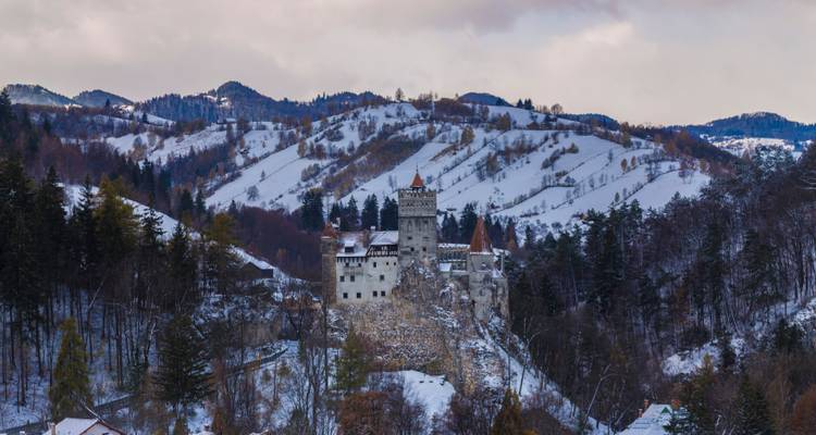 Colinas boscosas cubiertas de nieve que rodean el castillo de cuento de hadas de Bran bajo un cielo nublado