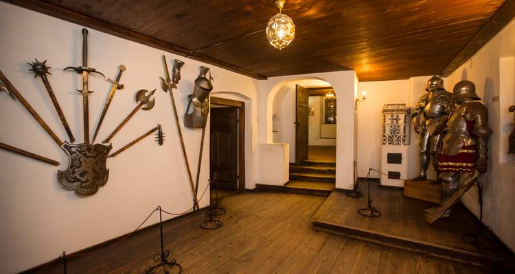 Exposición interior de armas y armaduras medievales exhibidas a lo largo de los pasillos de madera de un castillo