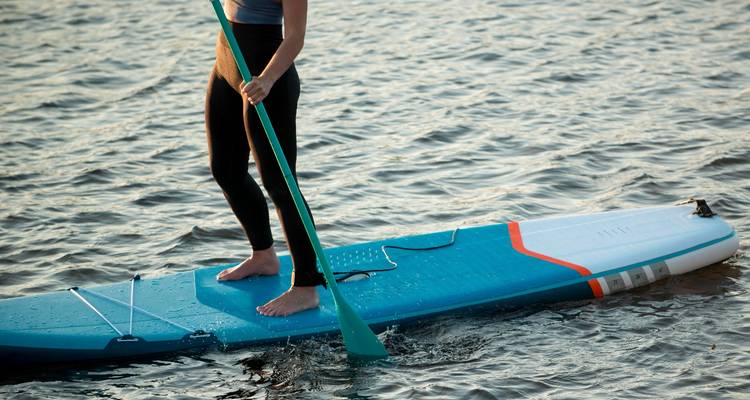 Close-up of person balancing on a blue stand-up paddleboard, paddle slicing the water