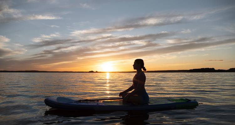 Silhouette of a person kneeling on paddleboard at sunset with colorful sky reflecting in the water