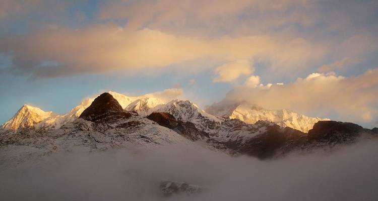 Schneebedeckte Berge mit tiefen Wolken und einem Sonnenuntergangshimmel.