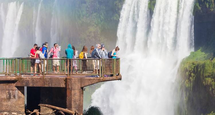 Turistas observando una gran cascada desde una plataforma de observación.