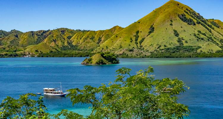 Serene view of a bay with a boat and lush green hills in the background.