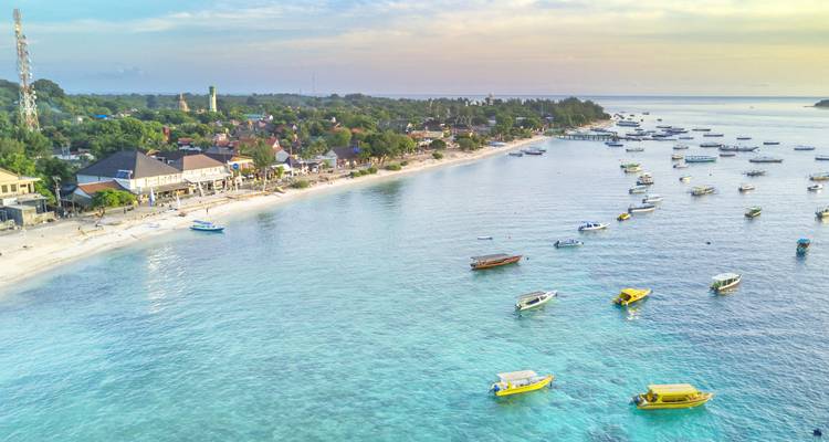 Aerial view of a beach lined with boats, turquoise water.