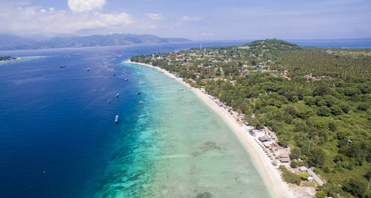 Aerial view of a long beach with blue waters and distant hills.