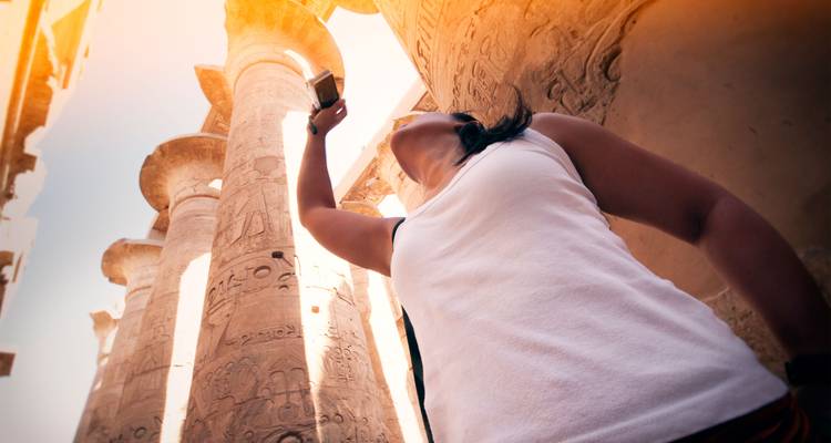 El viajero se recuesta para fotografiar columnas cubiertas de jeroglíficos bañadas en luz cálida.