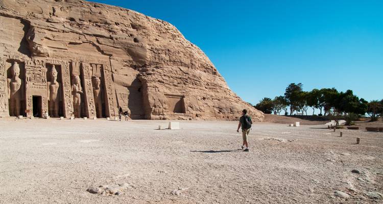 Un visitante se acerca a la fachada monumental tallada en roca de Abu Simbel bajo un cielo azul profundo.