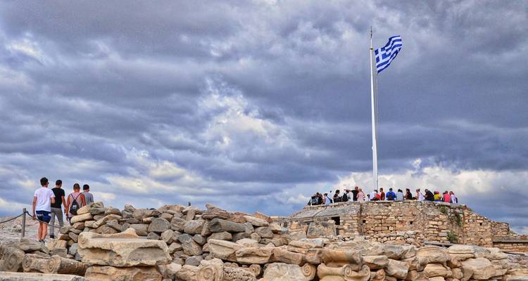 Des personnes se rassemblant sur une plateforme rocheuse avec un drapeau grec.