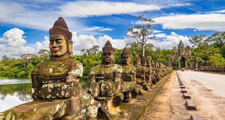 Oude stenen beelden op een brug die naar een tempel leidt.
