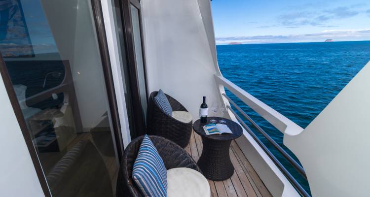 Private balcony on a cruise ship with chairs, table, and ocean view.