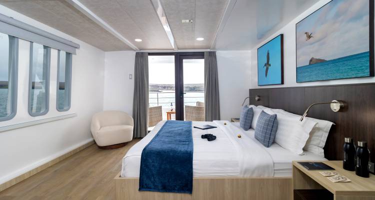 Spacious cruise ship cabin with bed, seating, and private balcony with ocean view.