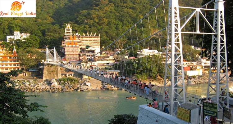 Suspension bridge full of people, with a river and green hills.