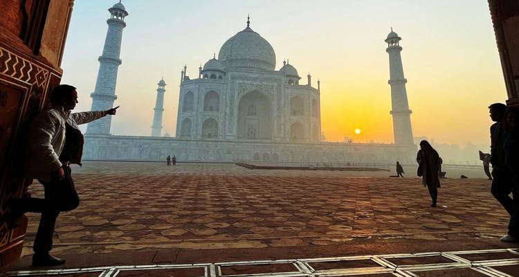 People silhouetted against the Taj Mahal at sunrise with a warm glow.