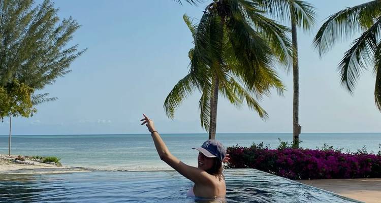 Woman in a pool with the ocean and palm trees in the background.
