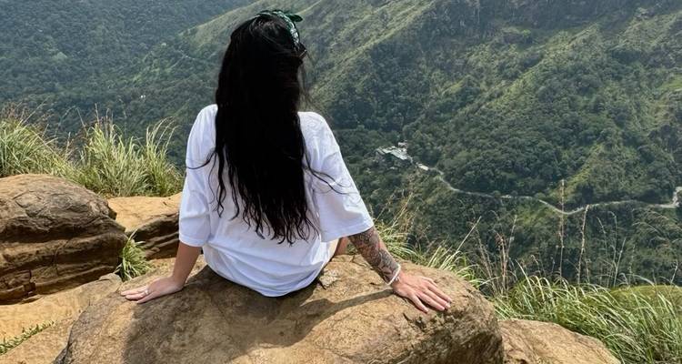 Woman sitting on a rock, overlooking a lush valley from high ground.