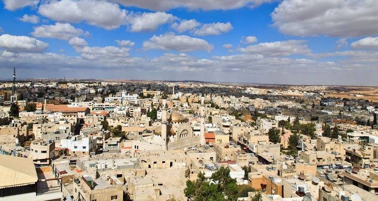 Vista panorámica sobre el pueblo de Madaba con edificios de piedra y cúpulas de iglesias bajo nubes dispersas.