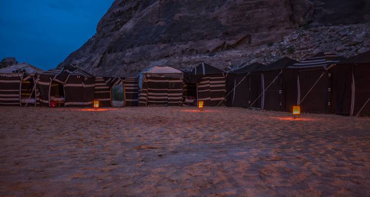 Fila de tiendas de campaña estilo beduino a rayas montadas en la arena del desierto al atardecer.