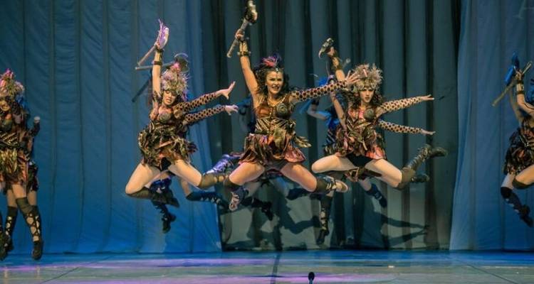 Danseurs en costumes d'inspiration tribale sautant sur scène.