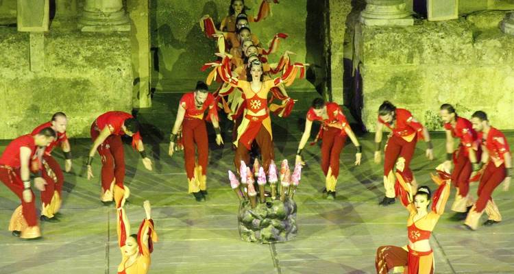 Troupe de danse folklorique colorée se produisant sur une scène de pierre ancienne sous un éclairage théâtral.