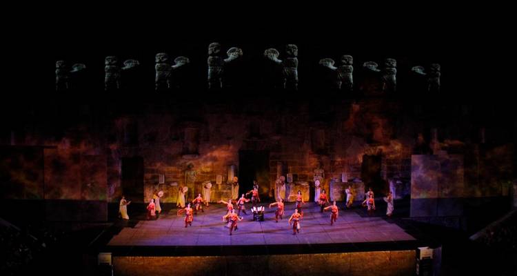 Plan large de nuit d'un spectacle sur scène dans un grand amphithéâtre antique avec des projections sur les murs.