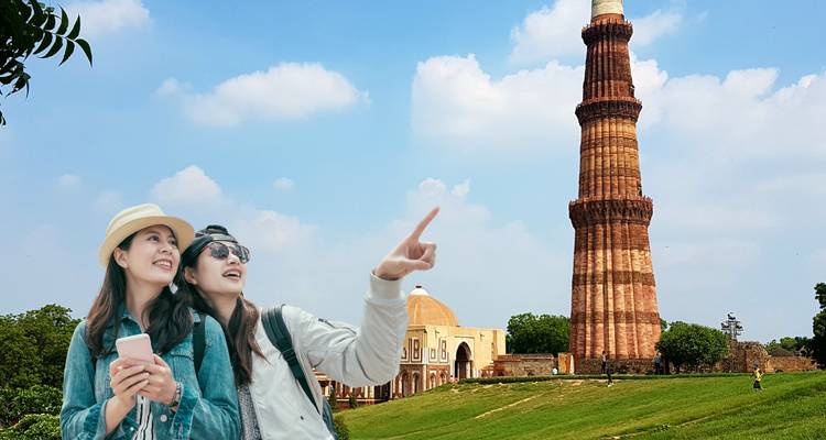 Tourists posing near Qutub Minar with a clear sky.