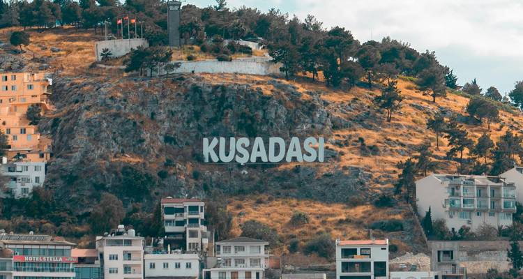 Letrero de Kusadasi en una ladera con edificios abajo.
