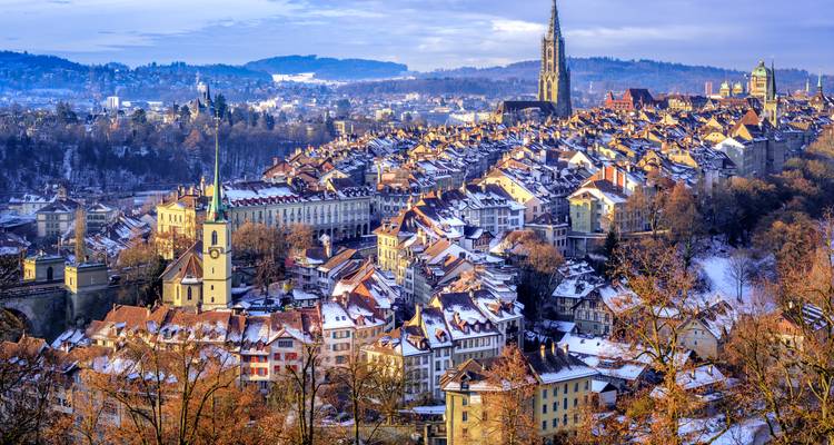 Schneebedeckte Stadtlandschaft mit einer markanten Kuppel und bewaldeten Hügeln.