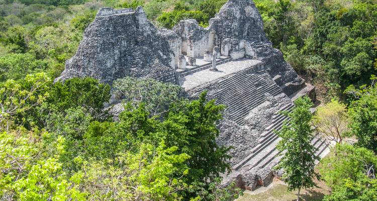 Ruinen einer antiken Pyramide, umgeben von Grün.